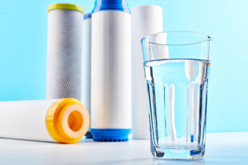 Water filters. Carbon cartridges and a glass on a white blue background. Household filtration...