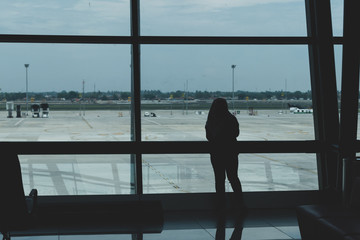 Fototapeta premium view of airport tarmac from within airport with person looking out of window