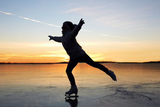 Cute little girl is skating on a frozen lake. Silhouette. Happy child playing on a winter walk in nature.