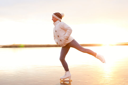 Cute little girl is skating on a frozen lake. Silhouette. Happy child playing on a winter walk in nature.