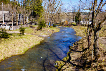 Fototapeta na wymiar Mountainous river flowing through small village. Early spring