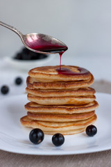 Stack of american pancakes with blackcurrant jam and fresh blackcurrant are lying on a white plate.