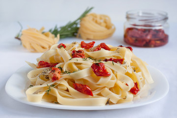 Fettuccine pasta with sun-dried tomatoes and fresh herbs are lying on a white plate. Isolated object.