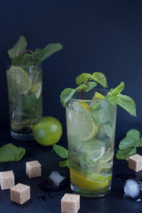 Two glasses of mojito cocktail with fresh lime and mint. Ice cubes and pieces of brown sugar are lying on a table.