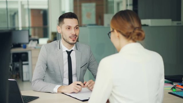 Smiling young man recruiter is talking to young woman successful candidate then shaking her hand during job interview in office. People and work concept.