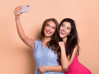 Two cheerful women taking selfie over pink background