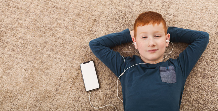 Boy in earphones listening to music lying on floor at home