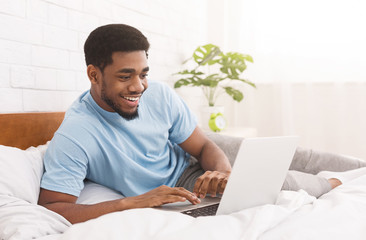 Black man lying in bed and watching something on laptop