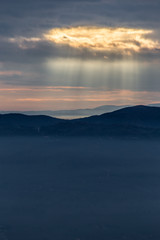 Sunray shines through clouds over the mountains and a sea of fog