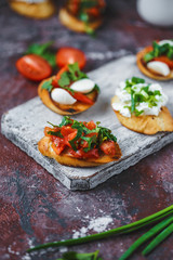 several types of italian bruschetta with tomatoes, mozzarella and herbs on a wooden board on a dark background