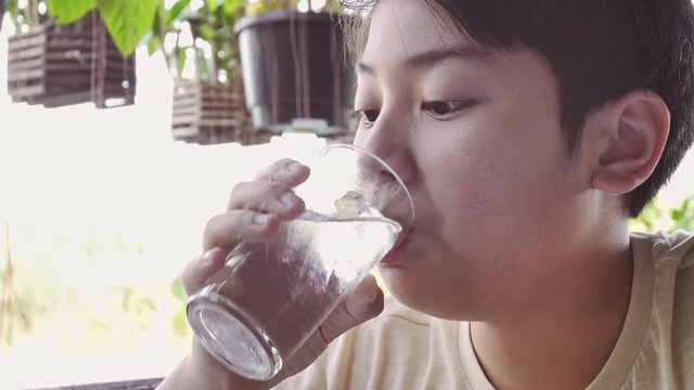 Slow motion of asian boy drinks water from a glass after breakfast, Close up teen boy with glass of water.