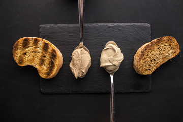 grilled bread with liver pate in spoon on stone plate on black background