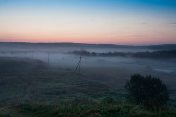 Fototapeta na wymiar The pre-dawn haze over the rural landscape with a power line A misty landscape in the early morning.
