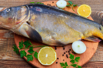 Raw carp fish with lemon, onion, pepper and parsley on cutting board on rustic wooden table