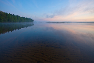 Dawn on the lake. In the foreground through the water you can see the sand