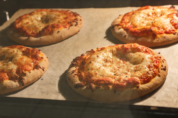 Four little pizza margherita with tomato sauce and mozzarella baking in the electric oven