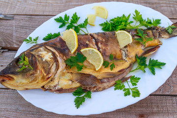 Baked carp fish with lemon and parsley on wooden table