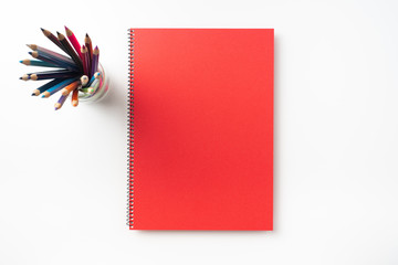 Top view of  red spiral notebook, page, pencil