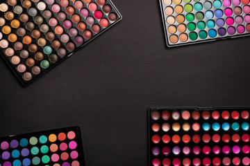 Flat lay of сolorful eyeshadow palettes on black background. Top view