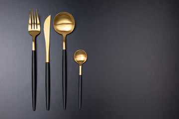 Set of black and gold cutlery on black background - obrazy, fototapety, plakaty