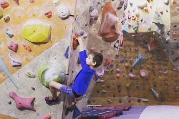 Fototapeta premium Little boy climbing a rock wall indoor.