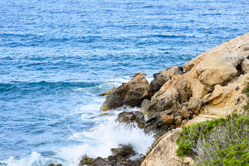 Fototapeta na wymiar The rocky coast of the Mediterranean sea during an afternoon surf. Background.