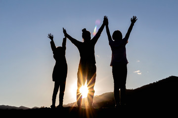 silhouette of people group with raised hands on the mountain at the sunset or sunrise time.