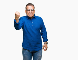 Middle age arab man wearing glasses over isolated background angry and mad raising fist frustrated and furious while shouting with anger. Rage and aggressive concept.