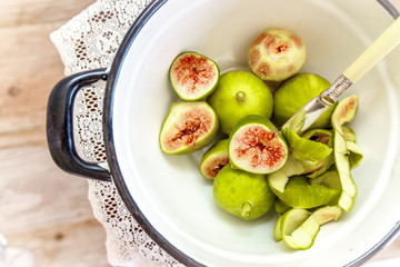 Cut ripe figs and antique knife in a vintage white enamel pot on an antique lace kitchen cloth and table
