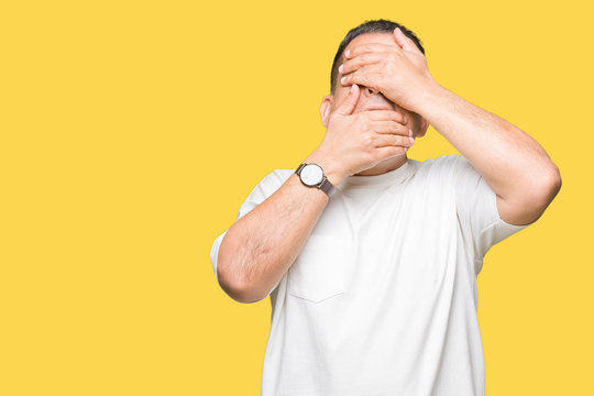 Middle age arab man wearig white t-shirt over isolated background Covering eyes and mouth with hands, surprised and shocked. Hiding emotion