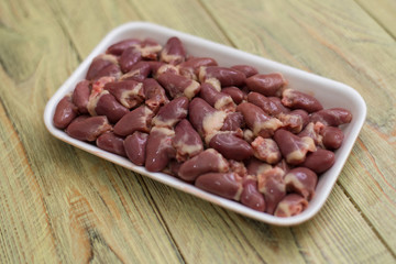 Raw chicken hearts in a tray on a wooden background.