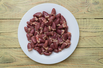 Raw chicken hearts on a white plate on a wooden background.