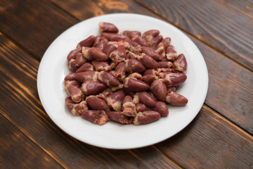 Raw chicken hearts on a white plate on a wooden background.