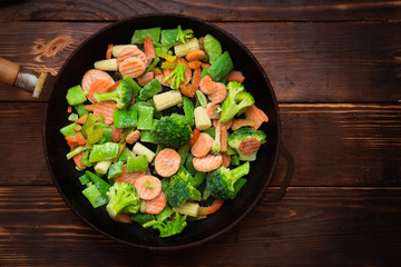 A mixture of frozen different vegetables in a pan on a wooden background.