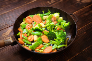 A mixture of frozen different vegetables in a pan on a wooden background.