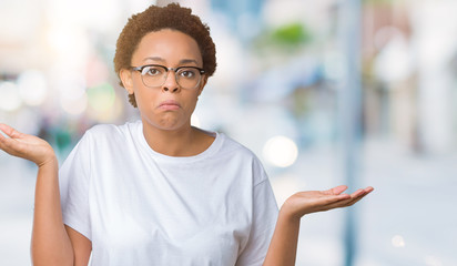 Beautiful young african american woman wearing glasses over isolated background clueless and confused expression with arms and hands raised. Doubt concept.