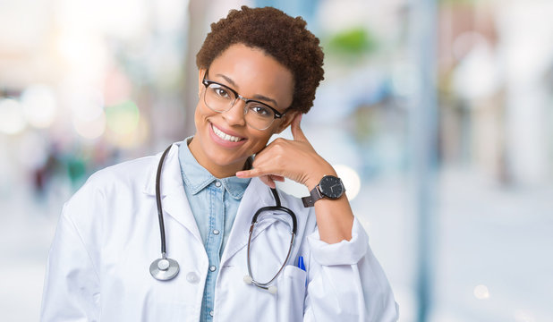 Young african american doctor woman wearing medical coat over isolated background smiling doing phone gesture with hand and fingers like talking on the telephone. Communicating concepts.