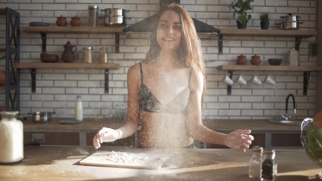 Smiling joyful pretty woman in lingerie claps her hands and powder flies. Ingredients and preparation stages. Slowmotion shot.