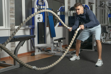 A boy is training with battle rope in gym
