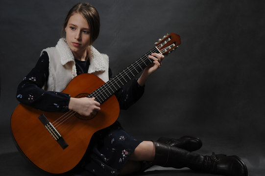 Girl with guitar. Studio light. Dark background.