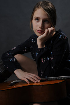 Girl with guitar. Studio light. Dark background.