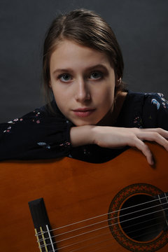 Girl with guitar. Studio light. Dark background.