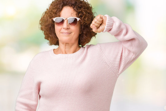 Beautiful middle ager senior woman wearing pink sweater and sunglasses over isolated background Strong person showing arm muscle, confident and proud of power