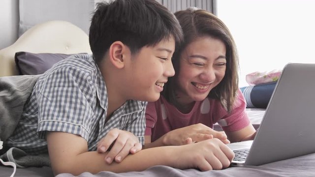 Happy family Mother and Son watching on laptop computer with smile face , Slow motion 4K  asian family rest on bed with laptop computer
