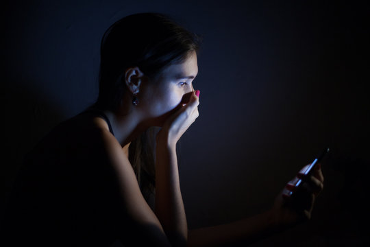 Teen Girl Excessively Sitting At The Phone At Home. He Is A Victim Of Online Social Networks. Sad Teen Checking Phone Sitting On The Floor In The Living Room At Home With A Dark Background.