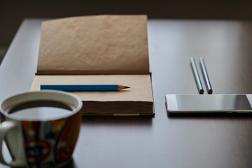 Recycled paper notebook, pencils, mobile phone and cup of coffee on a dark table. Work desk with a notebook with pencils, a smartphone and a cup of coffee.