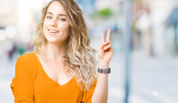 Beautiful young blonde woman over isolated background smiling with happy face winking at the camera doing victory sign. Number two.