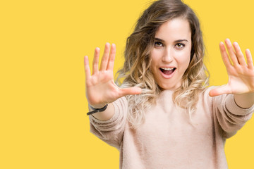 Beautiful young blonde woman wearing sweatershirt over isolated background afraid and terrified with fear expression stop gesture with hands, shouting in shock. Panic concept.