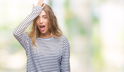 Beautiful young blonde woman wearing stripes sweater over isolated background surprised with hand on head for mistake, remember error. Forgot, bad memory concept.