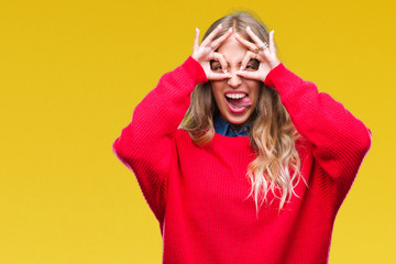 Beautiful young blonde woman wearing winter sweater over isolated background doing ok gesture like binoculars sticking tongue out, eyes looking through fingers. Crazy expression.